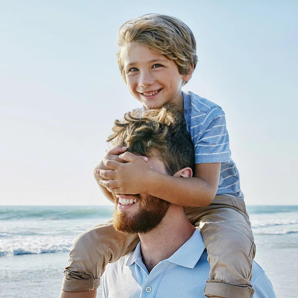 A man with a kid on his back strolls along the beach